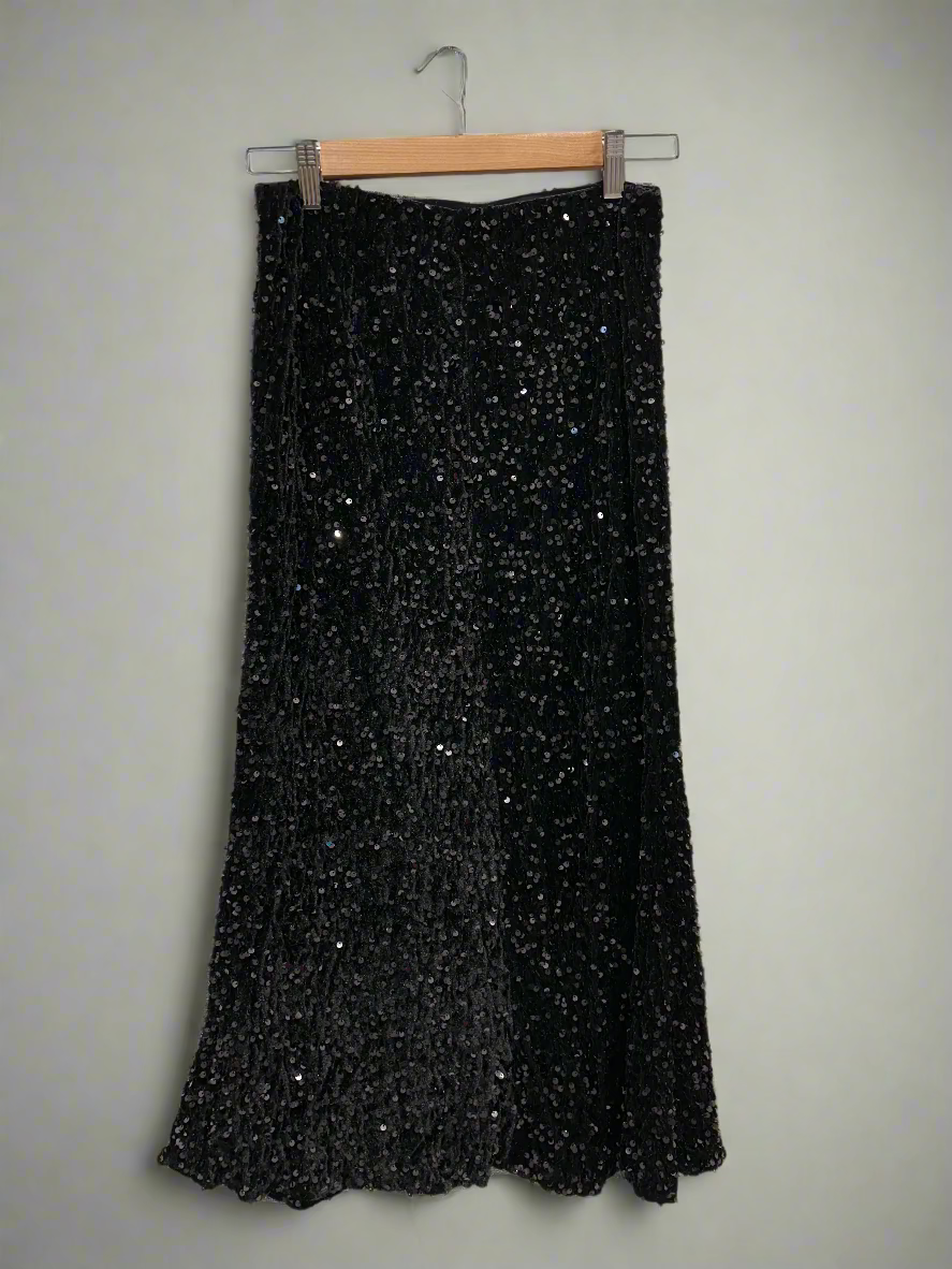 Black sequined skirt hanging against a white paneled wall.